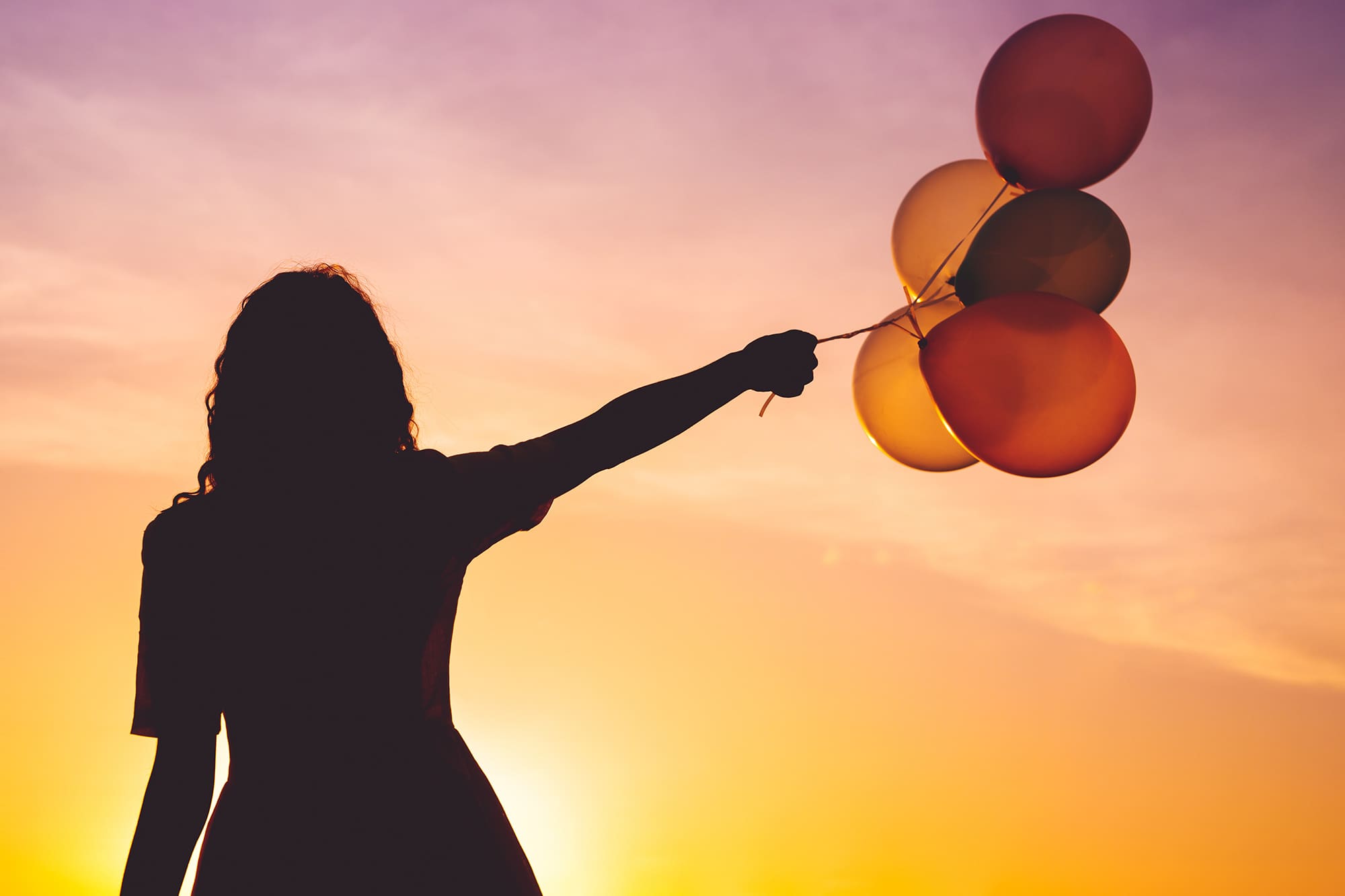 Dreamy woman carrying flying balloons in a colourful sky