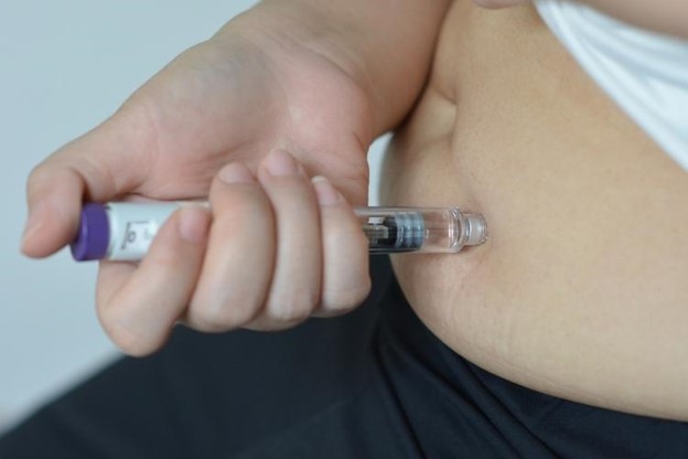 Self-administered subcutaneous injection into the abdomen using a syringe (close-up).