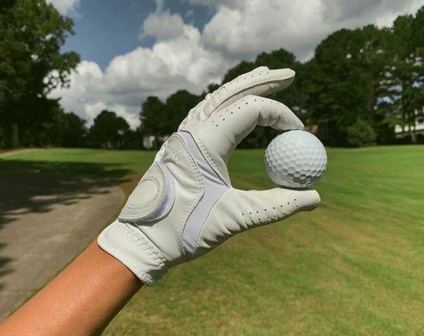 A hand wearing a white golf glove holding a golf ball
