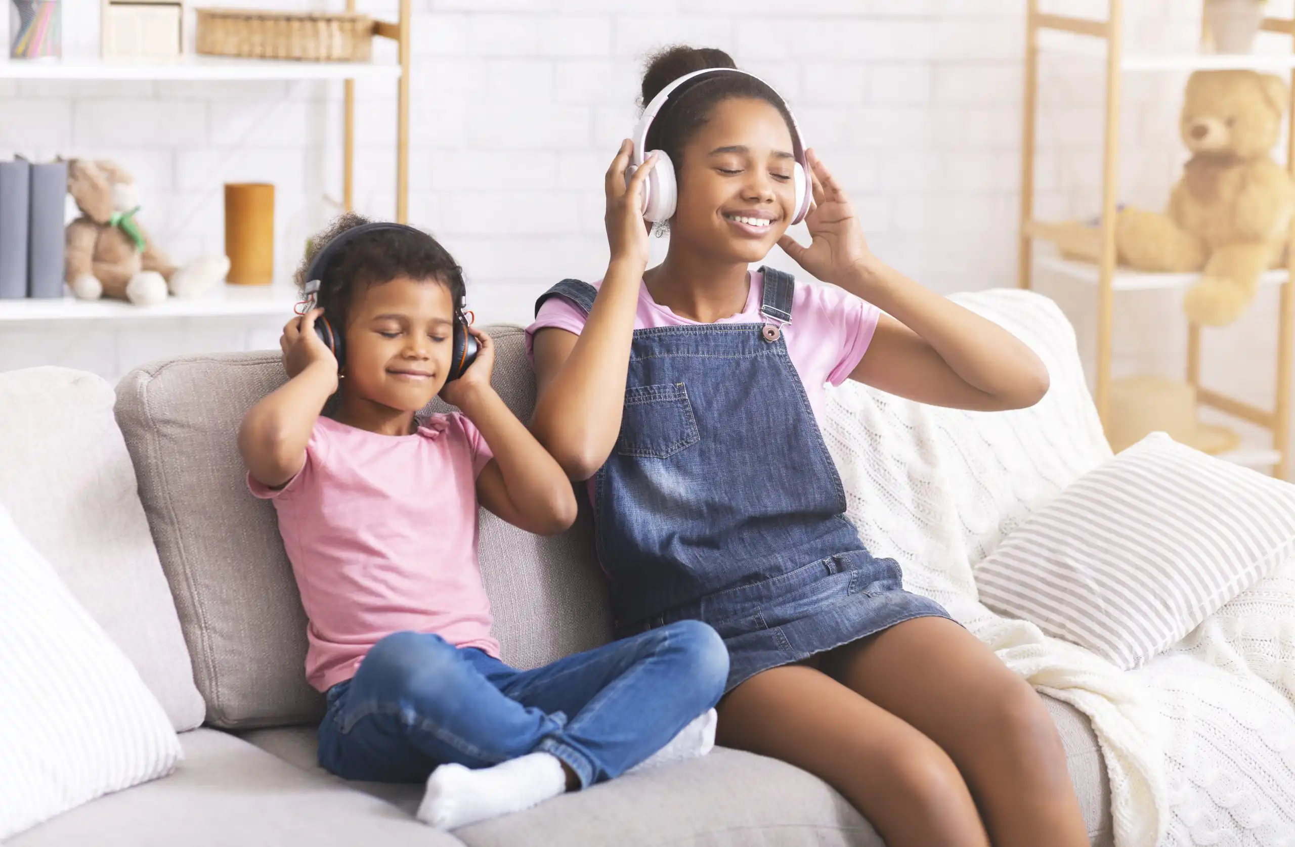 Two children wearing headphones on a sofa, smiling and enjoying music together in a cozy living room.