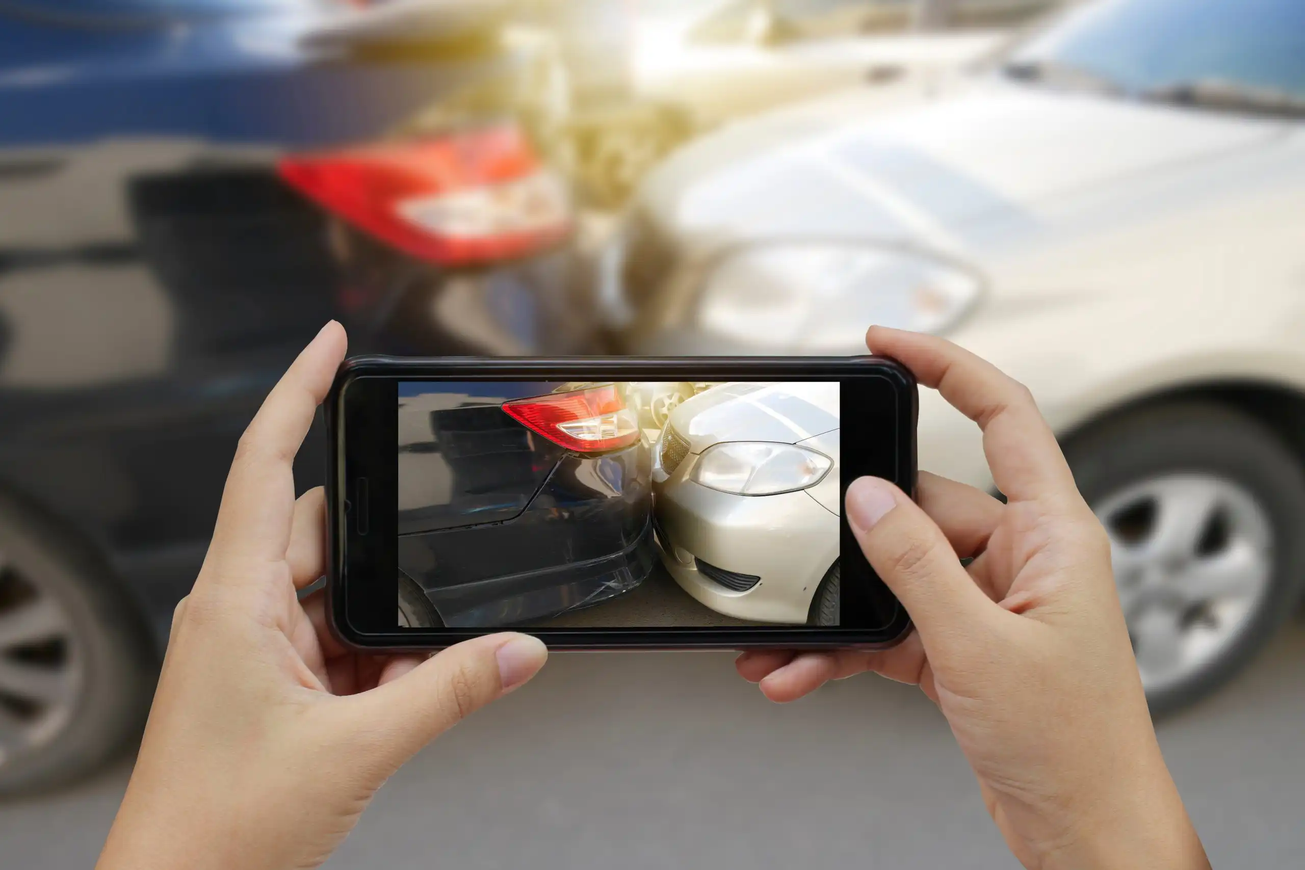 Hands hold a smartphone to photograph two cars' rear ends in a parking lot.