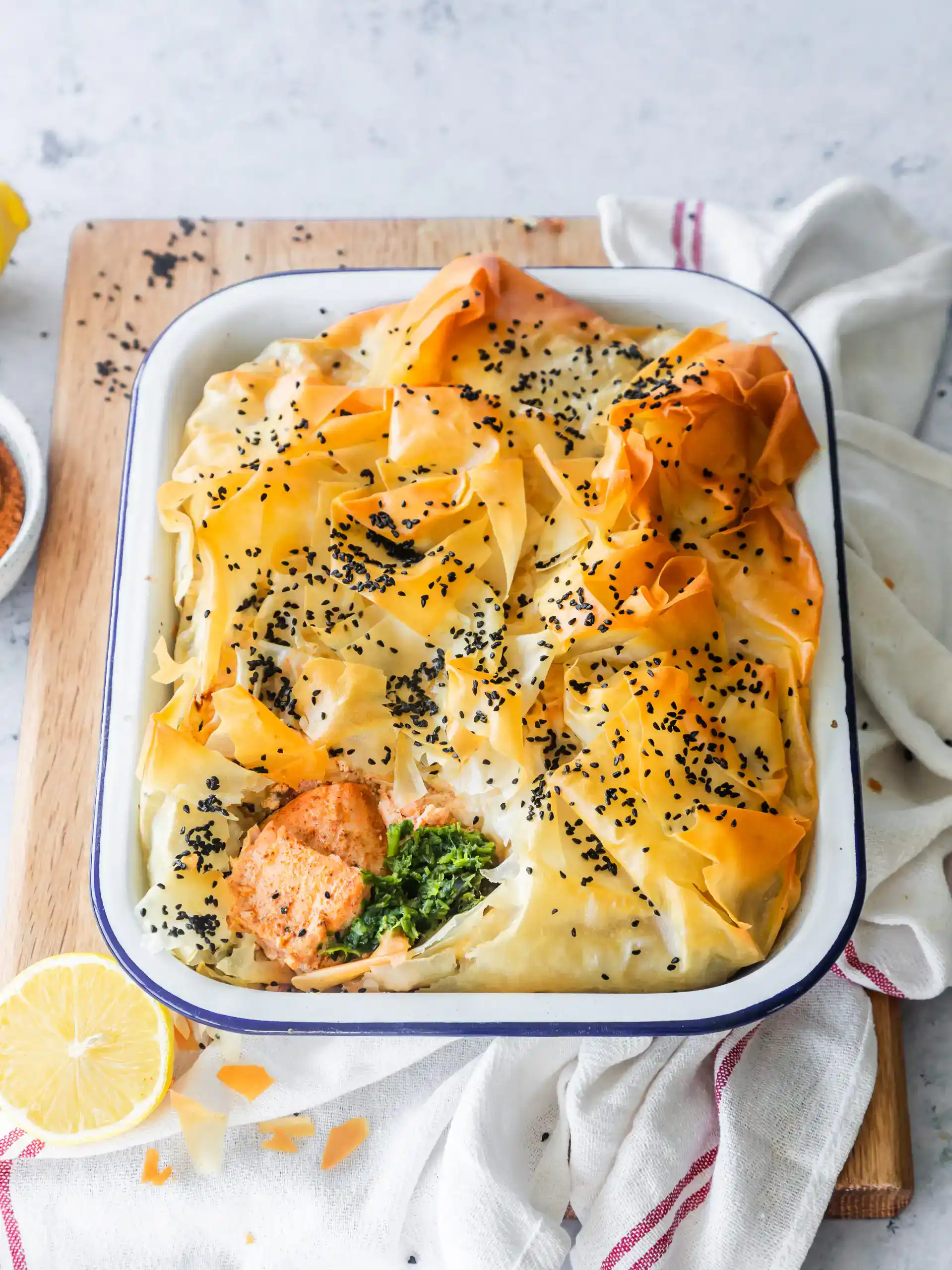 Baked vegetarian lasagna with pasta, cheese, and black sesame seeds in a white dish.