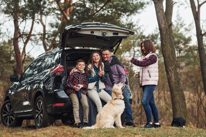 Family sitting in the boot of a car on a road trip with their dog